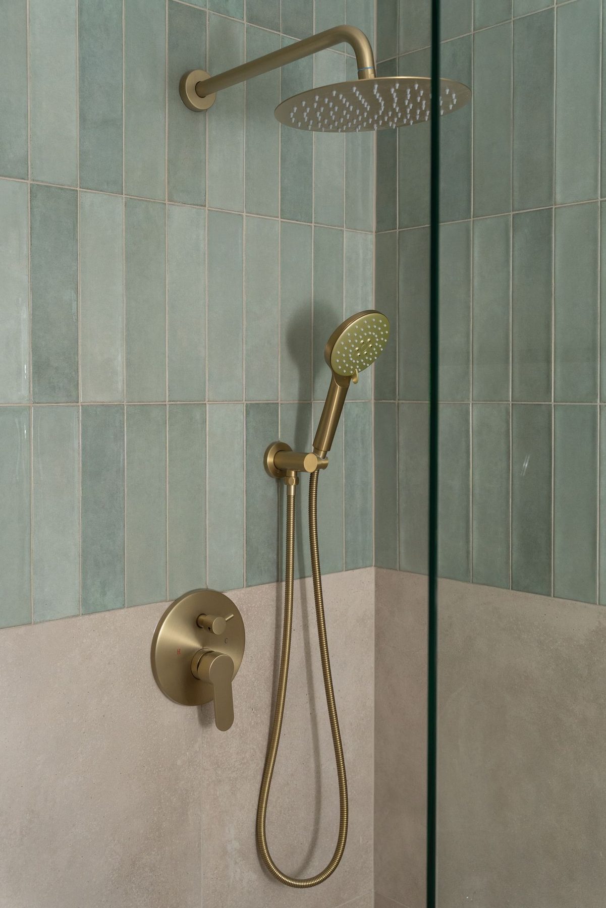 Primary washroom shower with soft green tile and brushed brass fixtures